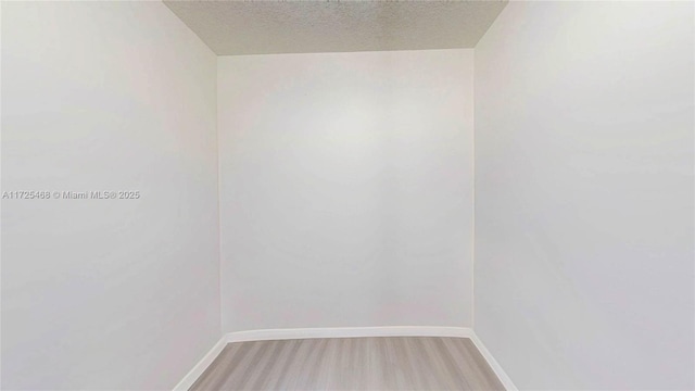 spare room featuring a textured ceiling, wood finished floors, and baseboards