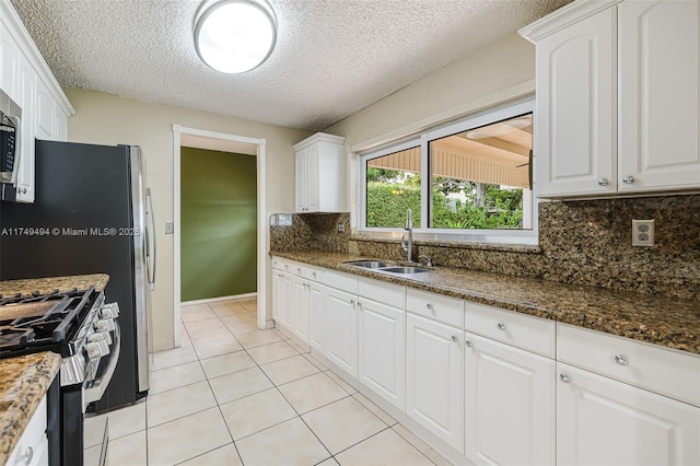 kitchen with light tile patterned floors, stainless steel appliances, backsplash, white cabinetry, and a sink