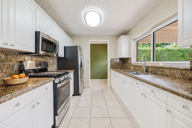 kitchen with stainless steel appliances, backsplash, white cabinets, light tile patterned flooring, and a sink