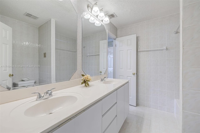 full bath featuring a textured ceiling, a sink, visible vents, and tile patterned floors