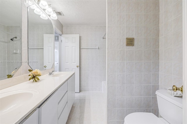 full bath featuring a tile shower, a sink, toilet, and tile walls