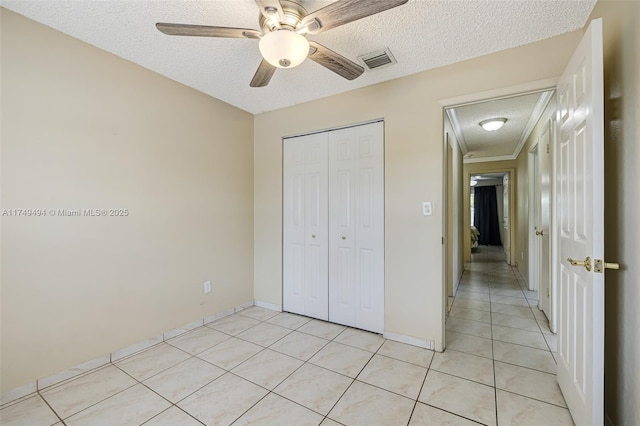 unfurnished bedroom featuring a textured ceiling, ceiling fan, light tile patterned floors, visible vents, and a closet