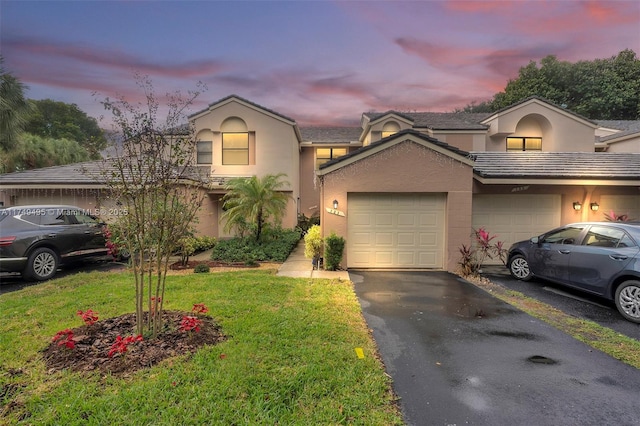 view of front facade with a garage, stucco siding, driveway, and a lawn