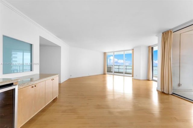 unfurnished living room featuring a wall of windows, beverage cooler, crown molding, and light wood-style flooring