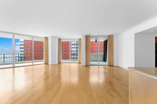 unfurnished room featuring plenty of natural light, expansive windows, crown molding, and wood finished floors