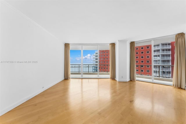 empty room featuring a city view, light wood finished floors, ornamental molding, a wall of windows, and baseboards