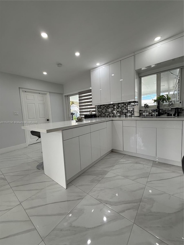 kitchen with a peninsula, white cabinets, light countertops, backsplash, and modern cabinets