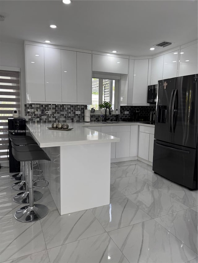 kitchen with white cabinetry, a peninsula, and black fridge