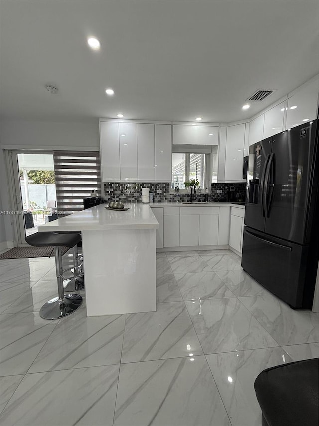 kitchen with a breakfast bar, modern cabinets, white cabinetry, and black fridge