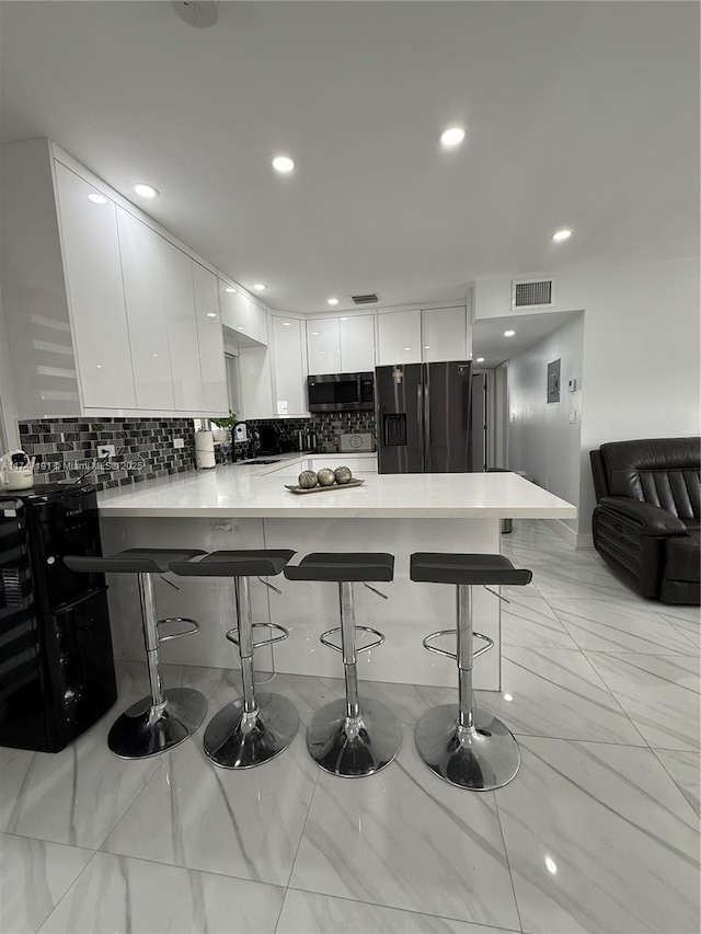 kitchen with a peninsula, a breakfast bar area, light countertops, and black fridge with ice dispenser