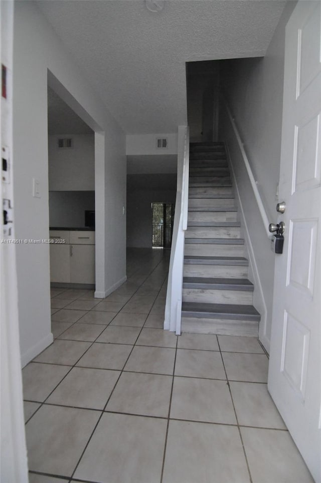 staircase with baseboards, visible vents, a textured ceiling, and tile patterned floors