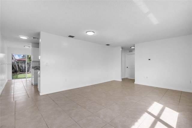 empty room with a textured ceiling, light tile patterned flooring, visible vents, and baseboards