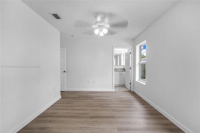 spare room with baseboards, visible vents, a ceiling fan, wood finished floors, and a textured ceiling