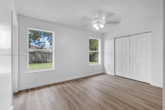 unfurnished bedroom with light wood-style flooring, a closet, baseboards, and a textured ceiling