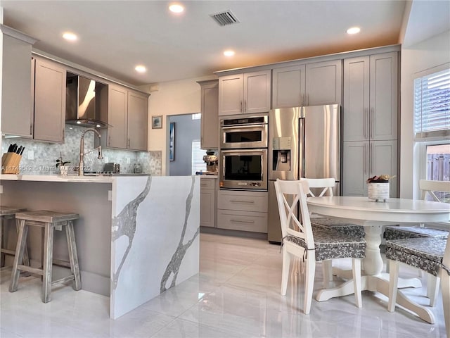 kitchen with wall chimney exhaust hood, appliances with stainless steel finishes, and gray cabinetry