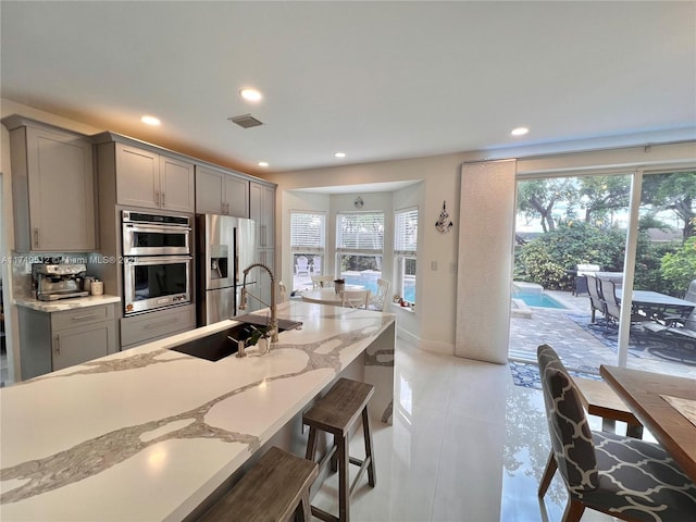 kitchen with visible vents, appliances with stainless steel finishes, light stone countertops, gray cabinets, and a sink