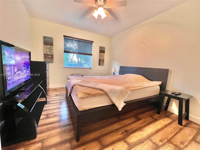 bedroom with a ceiling fan, a textured ceiling, baseboards, and wood finished floors