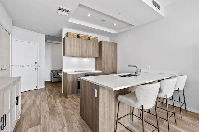 kitchen featuring brown cabinets, light countertops, visible vents, a sink, and light wood-type flooring