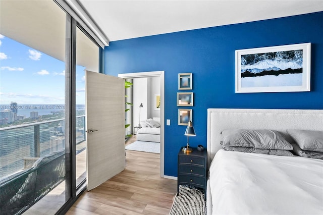 bedroom with light wood-type flooring, floor to ceiling windows, and a city view