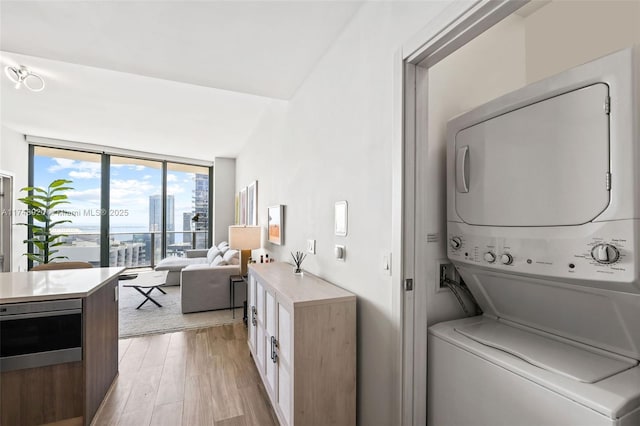 laundry room with a view of city, laundry area, stacked washing maching and dryer, and light wood-style flooring