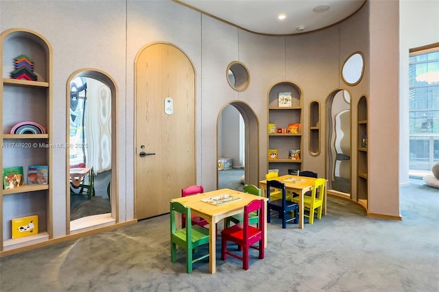 playroom featuring built in shelves, arched walkways, and carpet flooring