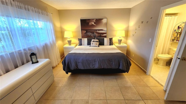 bedroom with ensuite bathroom, baseboards, and light tile patterned floors