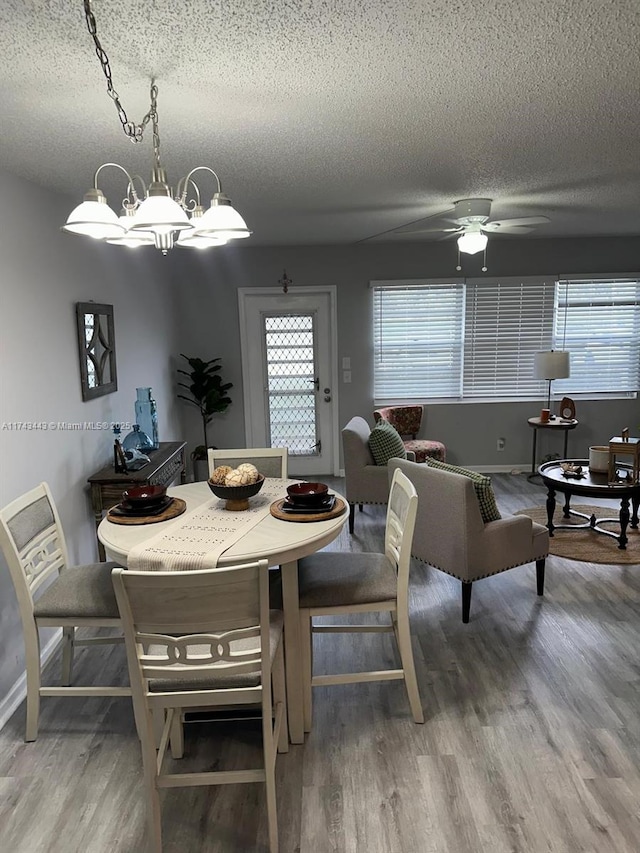 dining space with ceiling fan with notable chandelier, a textured ceiling, baseboards, and wood finished floors