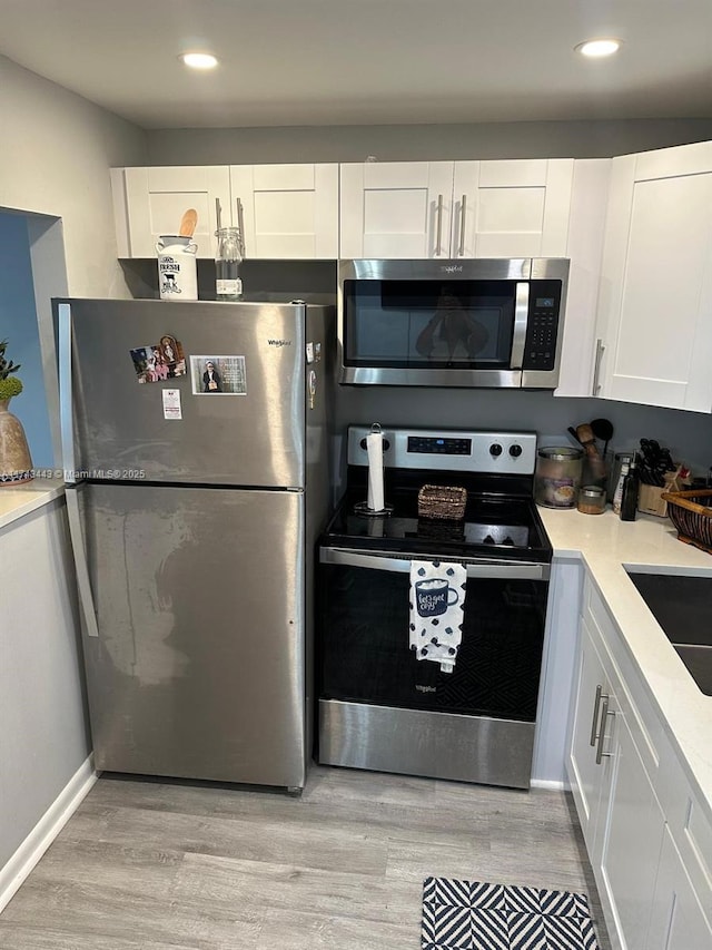 kitchen featuring light wood finished floors, white cabinetry, stainless steel appliances, and light countertops