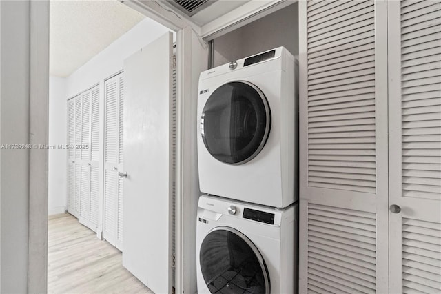 laundry room featuring stacked washer / drying machine, visible vents, laundry area, and light wood-type flooring