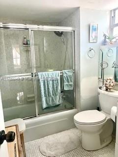 bathroom featuring toilet, combined bath / shower with glass door, and tile patterned floors