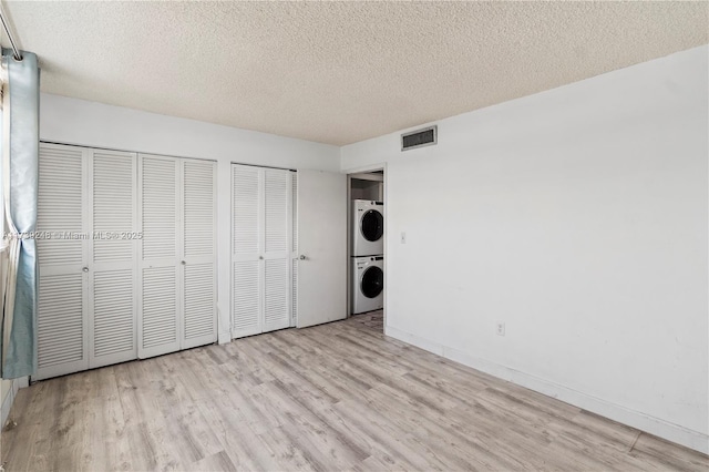 unfurnished bedroom with wood finished floors, a textured ceiling, multiple closets, stacked washer and dryer, and visible vents