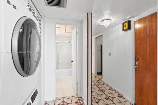 laundry room with light tile patterned floors, visible vents, baseboards, stacked washer and clothes dryer, and laundry area