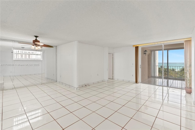 unfurnished room with a textured ceiling, a water view, light tile patterned flooring, ceiling fan, and expansive windows