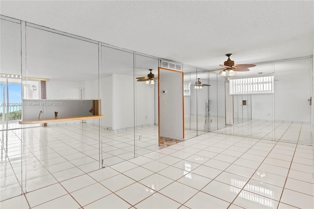 tiled empty room featuring a textured ceiling, visible vents, and ceiling fan