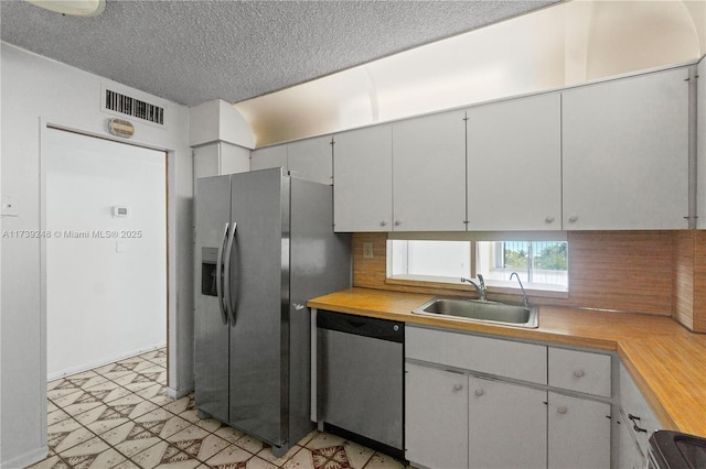 kitchen featuring a sink, stainless steel appliances, tasteful backsplash, visible vents, and light floors