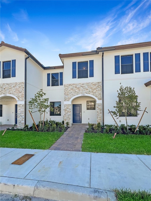 multi unit property featuring stone siding, a front yard, and stucco siding