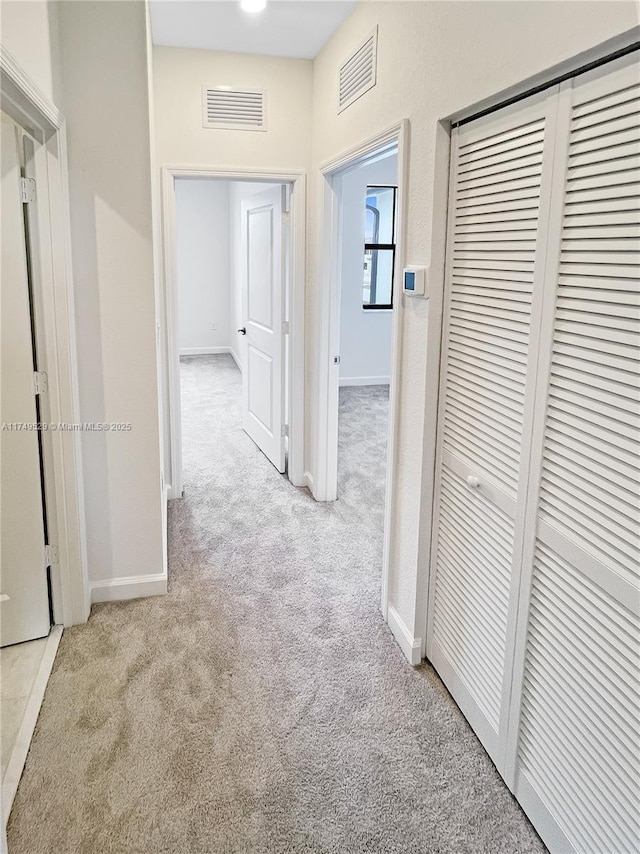 corridor with baseboards, visible vents, and light colored carpet