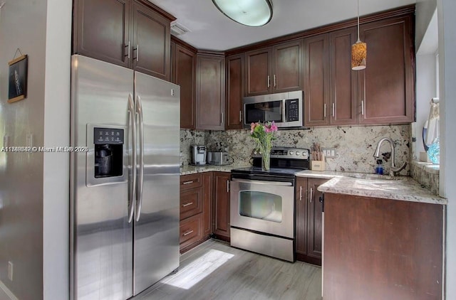 kitchen with appliances with stainless steel finishes, decorative light fixtures, backsplash, and light stone counters