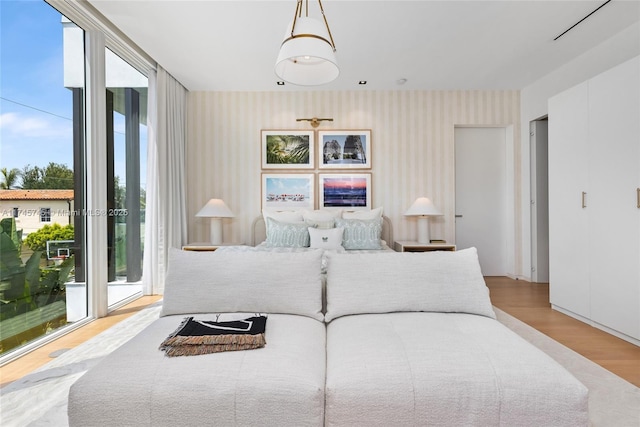 bedroom featuring floor to ceiling windows, light wood finished floors, and wallpapered walls