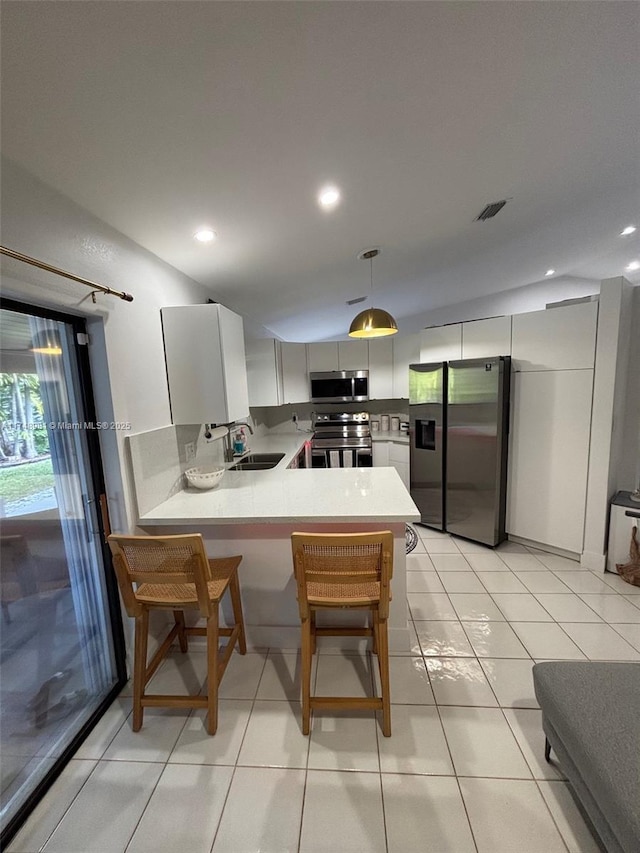 kitchen featuring appliances with stainless steel finishes, hanging light fixtures, a peninsula, light countertops, and white cabinetry