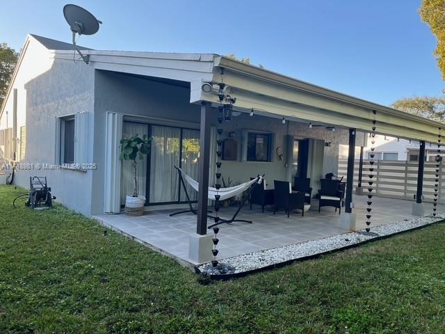 back of house with a patio area, a lawn, and stucco siding