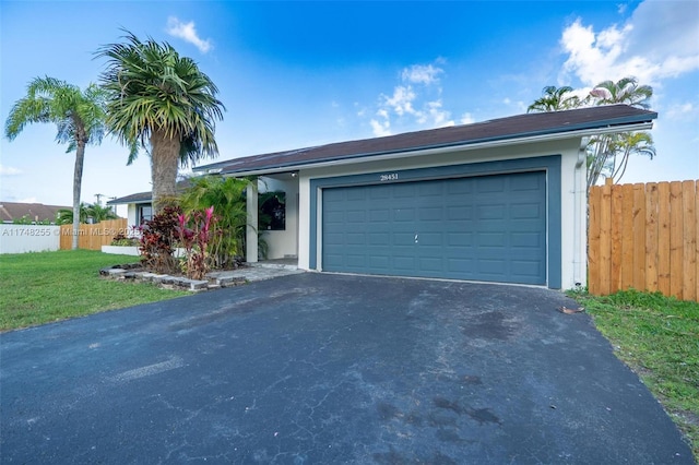 single story home featuring aphalt driveway, a front yard, fence, and a garage