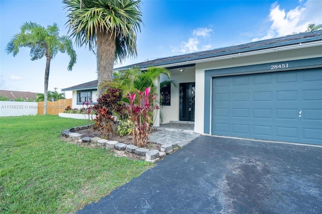 ranch-style home with driveway, a garage, fence, a front yard, and stucco siding