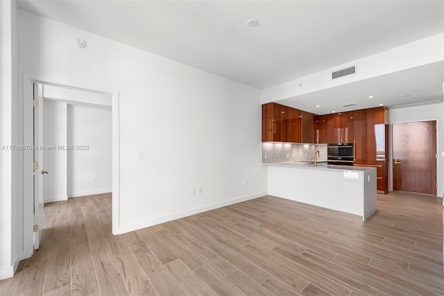 kitchen with brown cabinets, visible vents, decorative backsplash, modern cabinets, and a peninsula