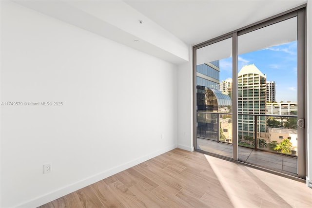 spare room with light wood finished floors, baseboards, a view of city, and floor to ceiling windows