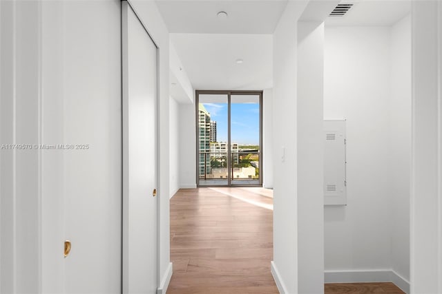 hallway with light wood-style flooring, visible vents, floor to ceiling windows, and baseboards