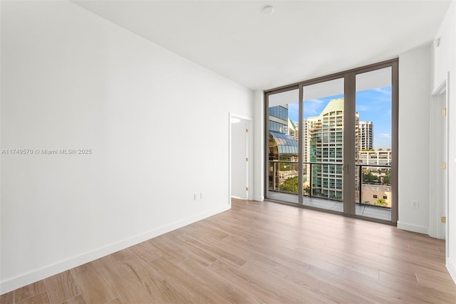 empty room featuring a view of city, light wood-type flooring, baseboards, and floor to ceiling windows