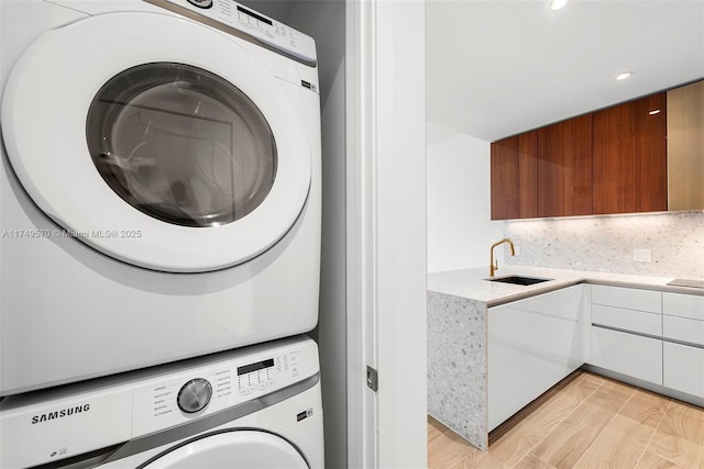 laundry room with laundry area, stacked washer / dryer, light wood-style flooring, a sink, and recessed lighting