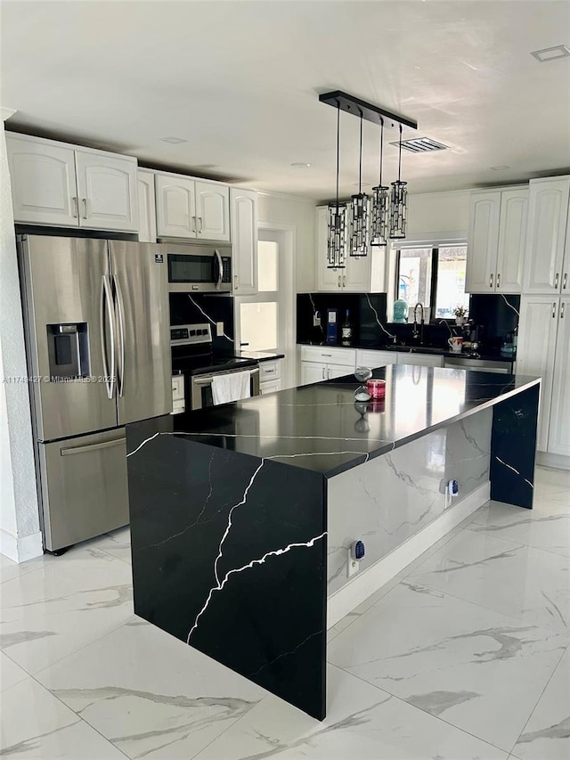 kitchen featuring white cabinets, appliances with stainless steel finishes, decorative light fixtures, and a center island