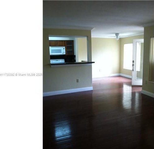 empty room with dark wood finished floors, crown molding, and baseboards